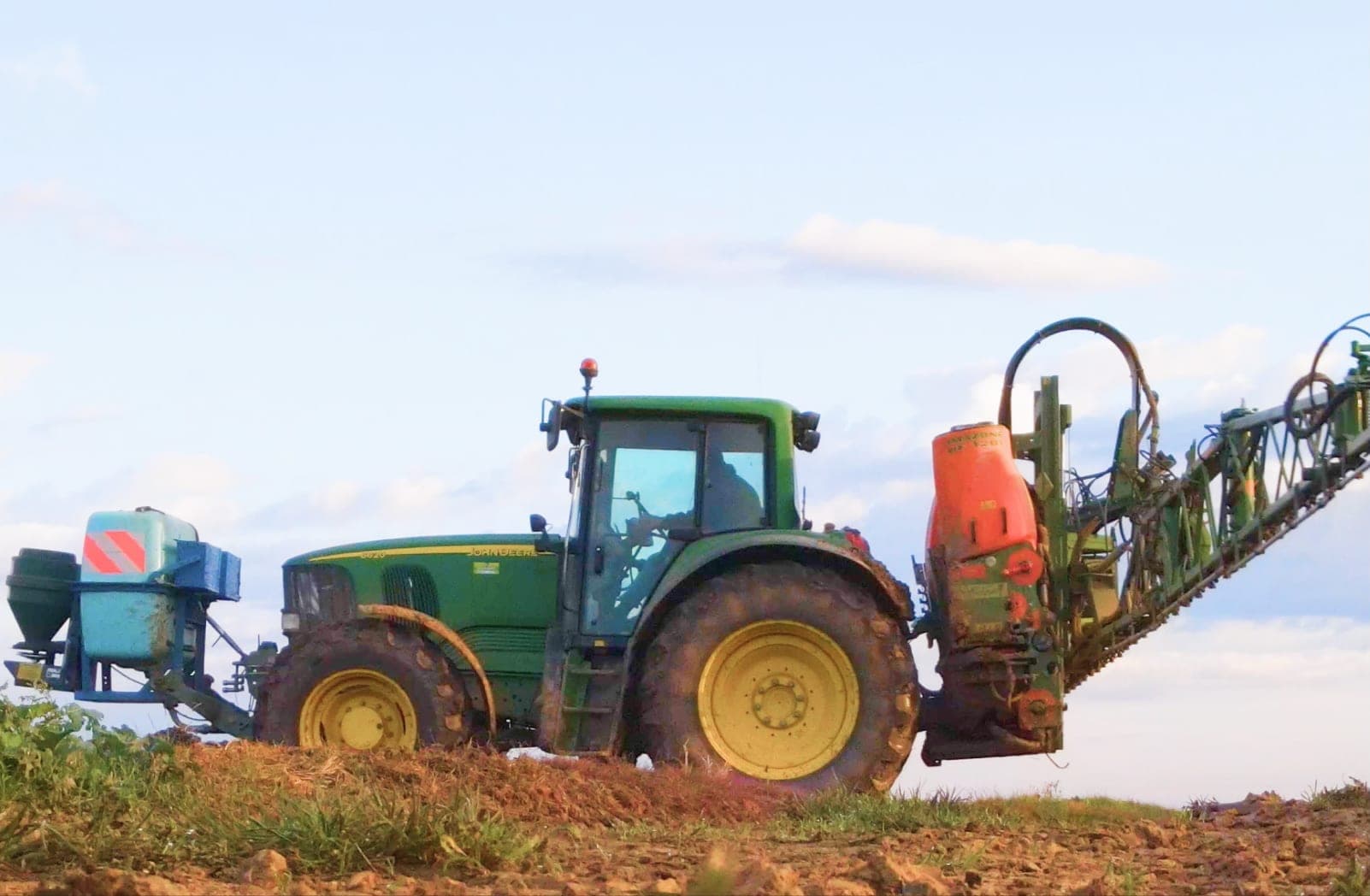 A tractor and boom sprayer working a field at dusk